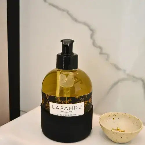 LAPAHDU Flüssigseife 250 ml in Glasflasche mit schwarzer Silikonhülle am Waschbecken, daneben ein kleines Schälchen mit Schmuck